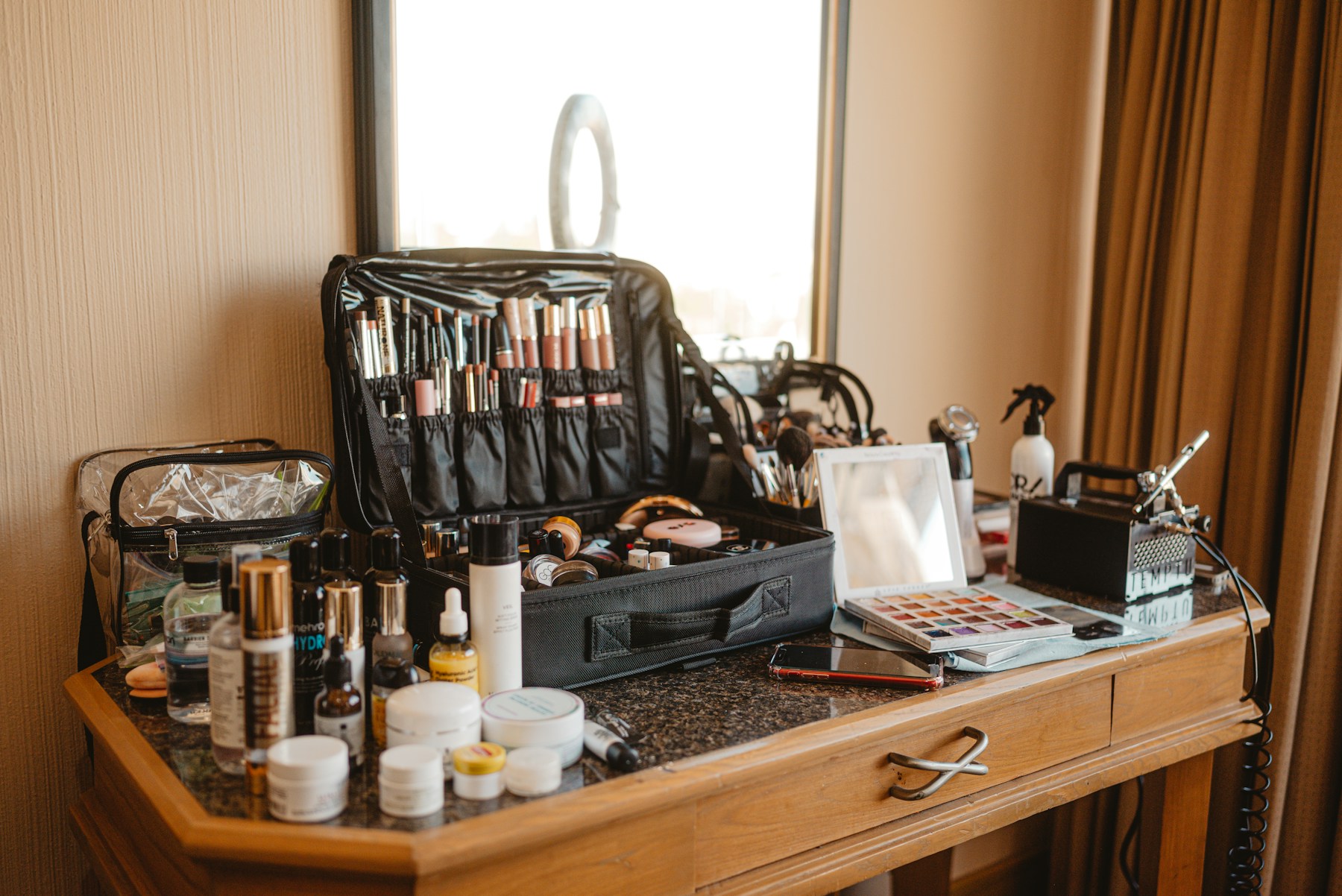 A makeup artist's cosmetics, palettes and brushes arranged across a wooden vanity table